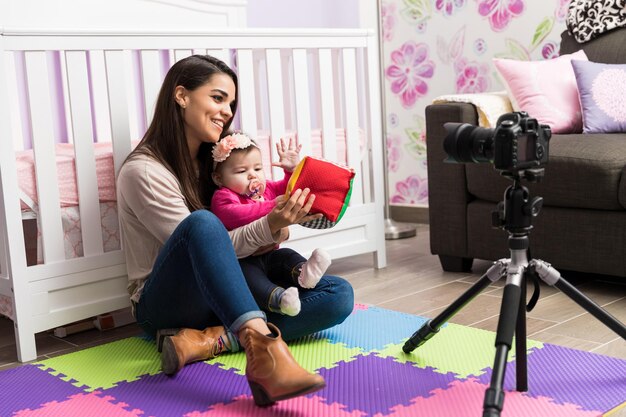 Jolie jeune blogueuse parentale enregistrant une vidéo avec son bébé à la maison