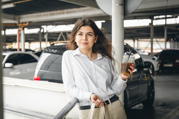 Photo gratuite jolie jeune femme d'affaires dans un parking avec une tasse de café