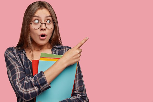 Jolie jeune femme d'affaires posant contre le mur rose avec des lunettes