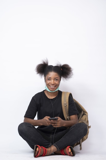 Jolie jeune femme africaine portant un sac à dos, les jambes assises croisées à l'aide de son téléphone portable