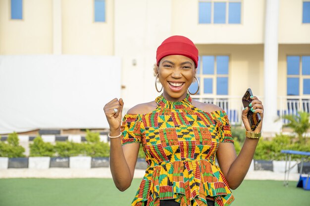 Jolie jeune femme africaine souriante tout en tenant son téléphone portable à l'extérieur