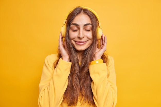 Jolie jeune femme apprécie l'atmosphère calme écoute de la musique via des écouteurs garde les yeux fermés