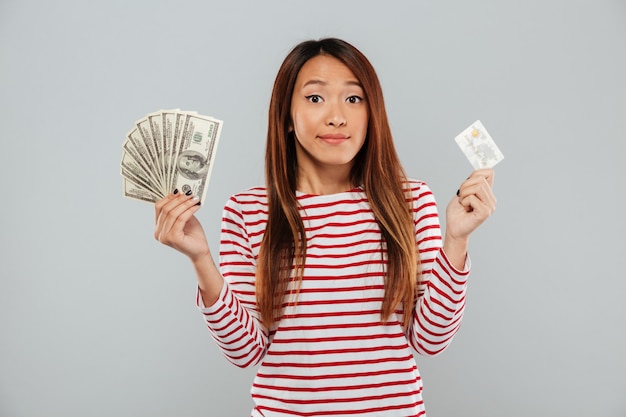 Jolie jeune femme asiatique détenant de l'argent et une carte de crédit.