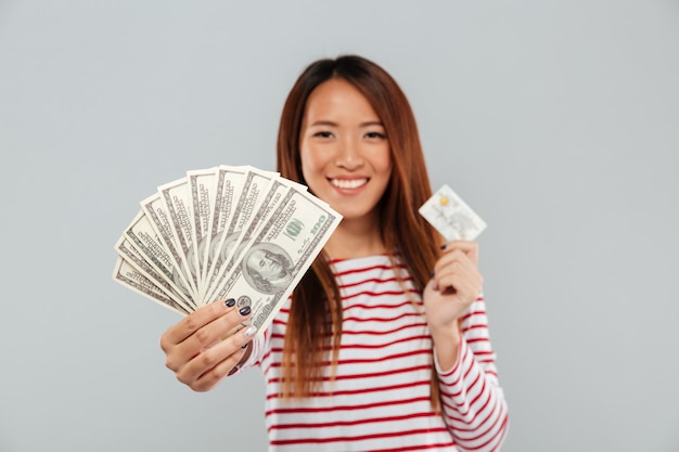 Jolie jeune femme asiatique détenant de l'argent et une carte de crédit.