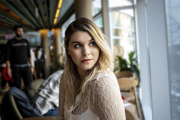 Jolie jeune femme assise dans un café à l'extérieur de la fenêtre