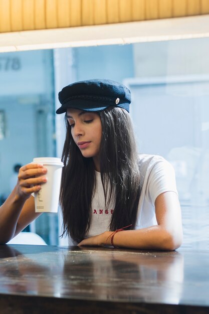 Une jolie jeune femme assise dans un café en regardant une tasse de café à emporter dans la main