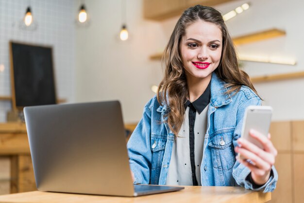 Jolie jeune femme assise dans un restaurant en regardant un téléphone mobile