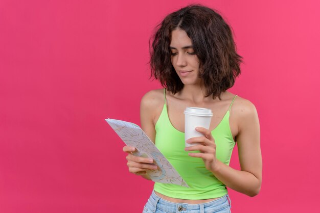 Une jolie jeune femme aux cheveux courts en vert crop top holding tasse en plastique de café en regardant la carte