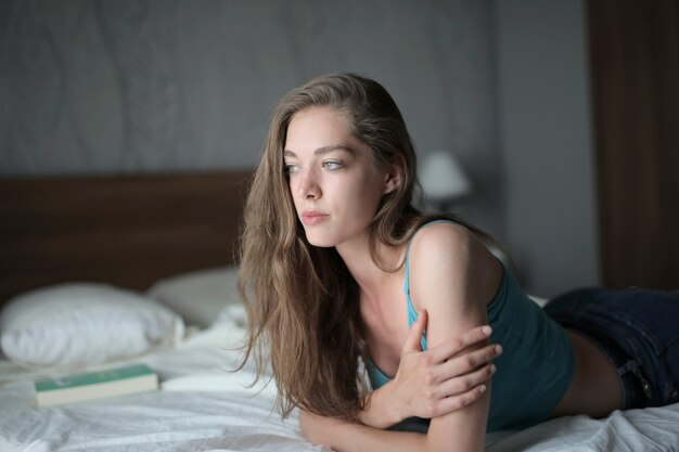Jolie jeune femme aux cheveux longs allongée sur le lit sous les lumières dans une pièce