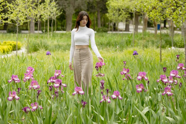 Jolie jeune femme ayant une séance photo dans un parc fleuri touchant des fleurs à la main