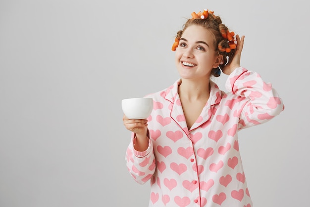 Jolie Jeune Femme En Bigoudis Et Pyjamas Buvant Le Café Du Matin