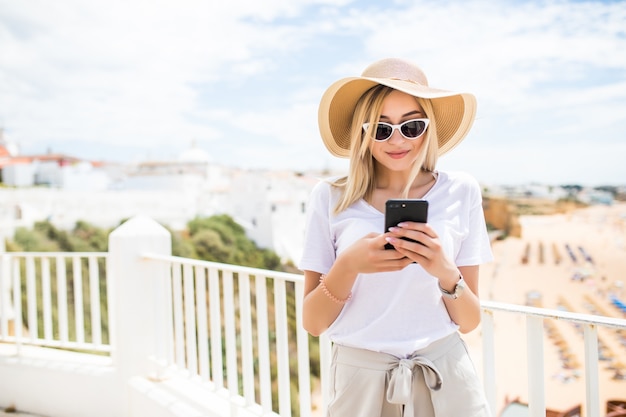 Jolie jeune femme blonde en tapant sur le téléphone sur la terrasse sur la plage