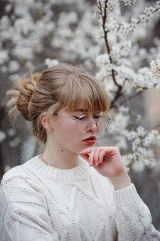 Jolie jeune femme dans un chandail blanc dans le jardin de fleurs de cerisier, printemps