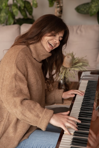 Jolie jeune femme dans un pull marron confortable joue du piano.