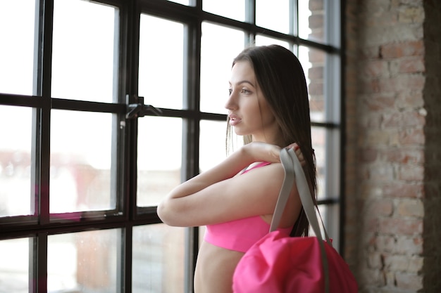 Jolie jeune femme dans une tenue de gym tenant son sac et regardant à l'extérieur de la fenêtre