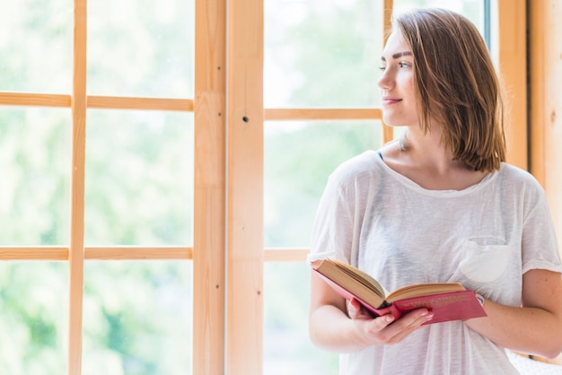 Photo gratuite jolie jeune femme debout devant le livre de tenue de fenêtre