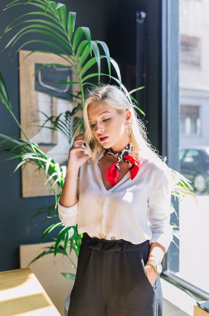 Une jolie jeune femme debout près de la fenêtre parlant au téléphone avec sa main dans la poche