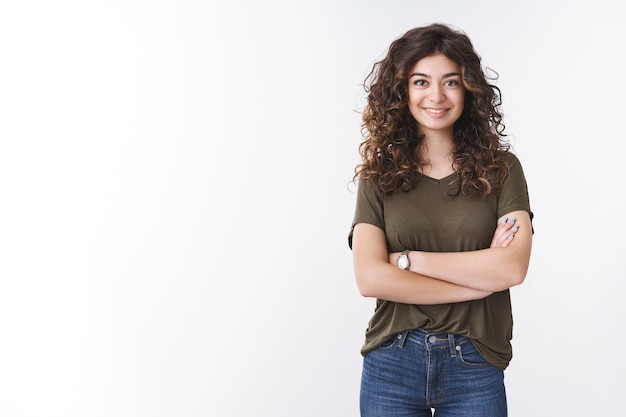 Jolie jeune femme diatologue confiante et réussie avec les cheveux bouclés, les bras croisés, la poitrine sûre d'elle, prête à donner des conseils utiles, souriante, se sentant largement chanceuse, debout sur fond blanc