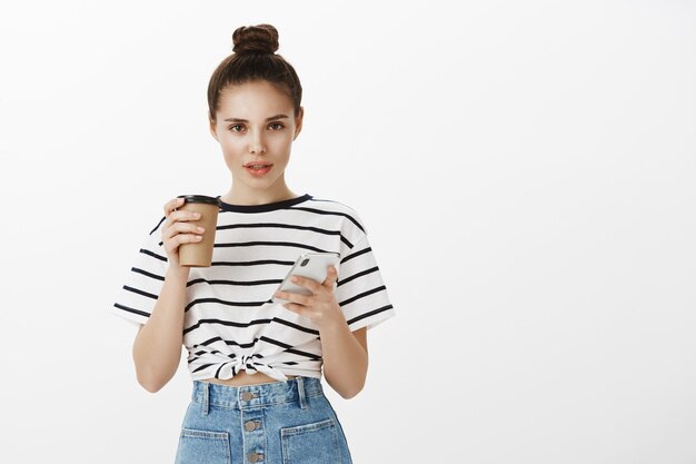 Jolie jeune femme élégante à l'aide de smartphone et de boire du café au café