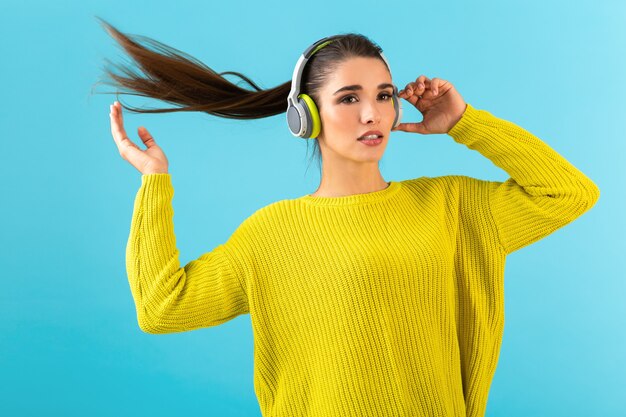 Jolie jeune femme élégante écoutant de la musique dans des écouteurs sans fil heureux portant chandail tricoté jaune