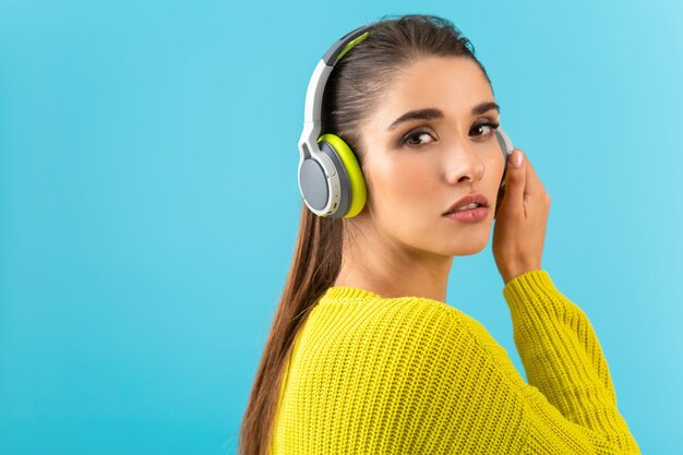 Jolie jeune femme élégante écoutant de la musique dans des écouteurs sans fil heureux portant un pull en tricot jaune style coloré posant