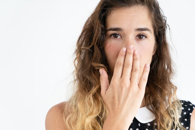 Jolie jeune femme embarrassée couvrant la bouche avec la main et regardant la caméra.