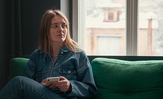 Une jolie jeune femme est assise sur le canapé près de la fenêtre