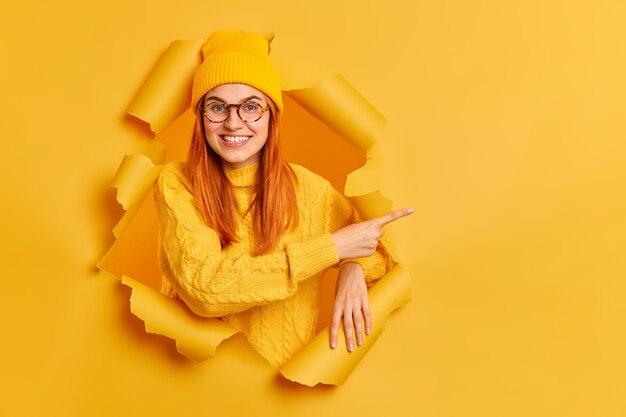 Jolie jeune femme avec une expression joyeuse pointant sur le côté du trou de papier déchiré