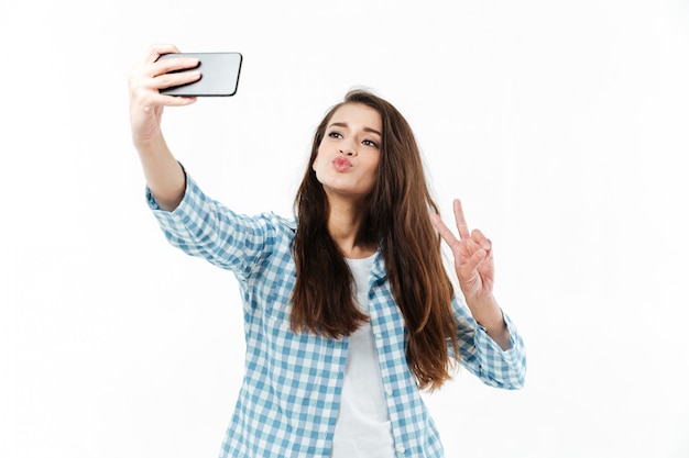 Jolie jeune femme faisant selfie et montrant le geste de la victoire