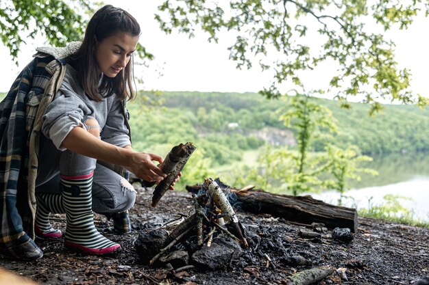 Une jolie jeune femme fait un feu pour se réchauffer dans la forêt.