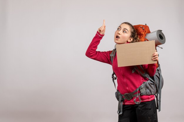Jolie jeune femme avec un gros sac à dos brandissant un doigt pointé en carton vers le haut