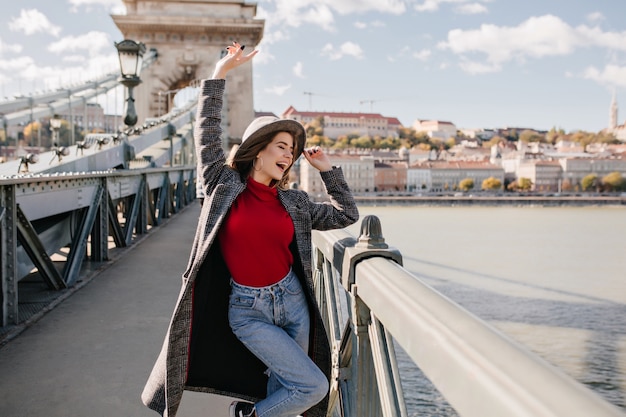 Jolie jeune femme en jeans et long manteau dansant sur le pont près de l'arc de triomphe