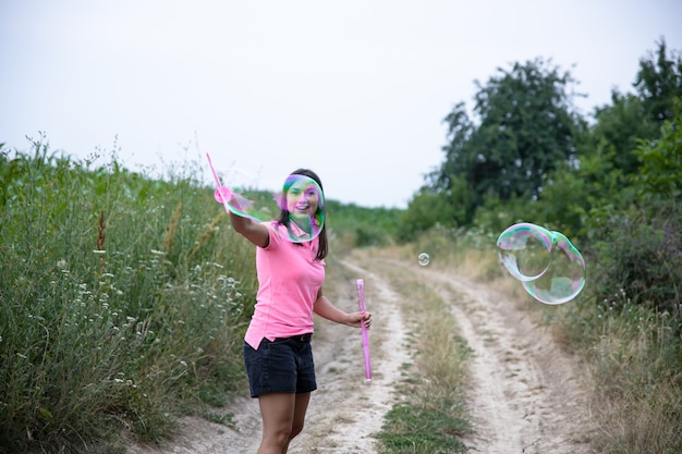 Une jolie jeune femme lance d'énormes bulles de savon en arrière-plan belle nature.