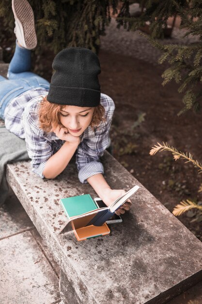 Jolie jeune femme lisant un livre sur un banc de pierre