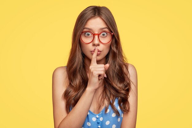 Jolie jeune femme avec des lunettes posant contre le mur jaune