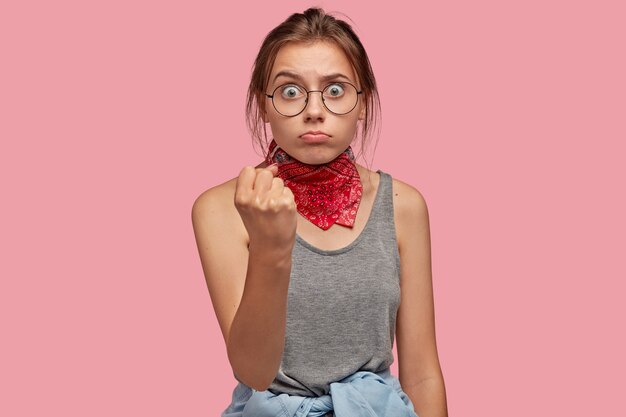 Jolie jeune femme avec des lunettes posant contre le mur rose