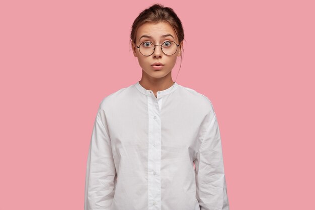 Jolie jeune femme avec des lunettes posant contre le mur rose