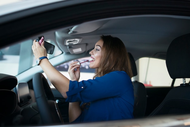 Jolie jeune femme mettant du rouge à lèvres dans une voiture