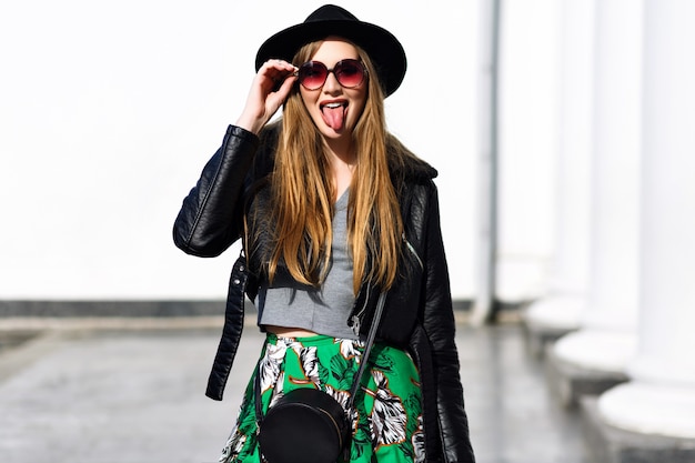 Jolie jeune femme à la mode aux cheveux longs, lunettes de soleil, chapeau noir à la recherche de soleil, marchant dans la rue en matinée ensoleillée. Modèle élégant, perspectives de luxe, exprimant de vraies émotions