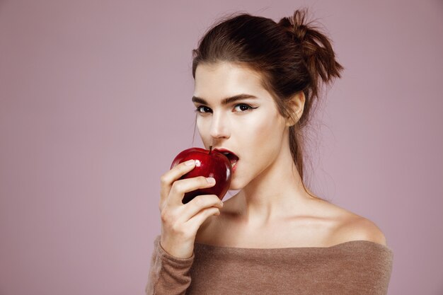 Jolie jeune femme mordant une pomme rouge sur rose