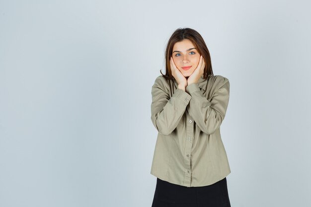 Jolie jeune femme oreiller visage sur ses mains en chemise, jupe et à la honte, vue de face.