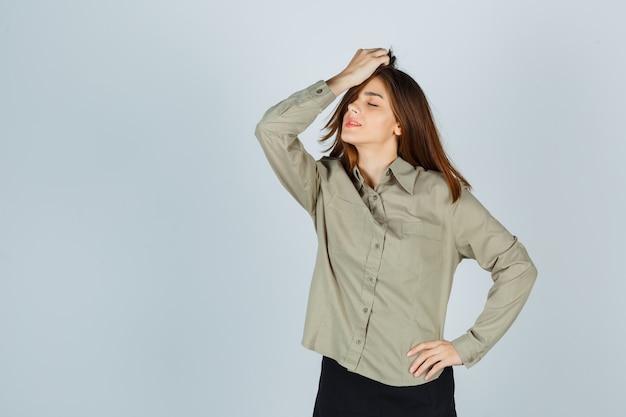 Jolie jeune femme peignant les cheveux en chemise, jupe et l'air détendu, vue de face.