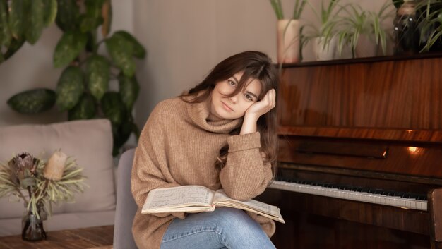 Une jolie jeune femme pianiste dans un chandail confortable est assise près d'un piano avec des notes.