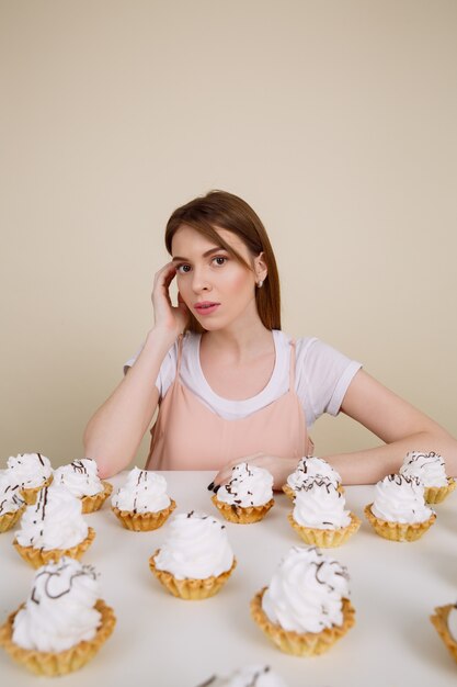 Jolie jeune femme posant assis près de cupcakes sur table