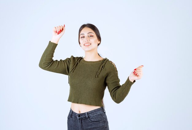 Jolie jeune femme posant joyeusement sur le mur blanc