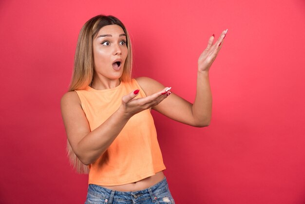 Jolie jeune femme regardant de façon choquante son côté sur le mur rouge.