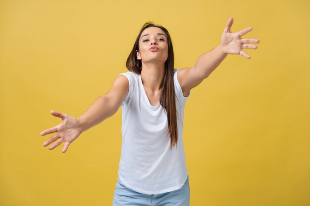 Jolie jeune femme rêveuse heureuse en t-shirt blanc isolé sur fond jaune donnant un baiser aérien