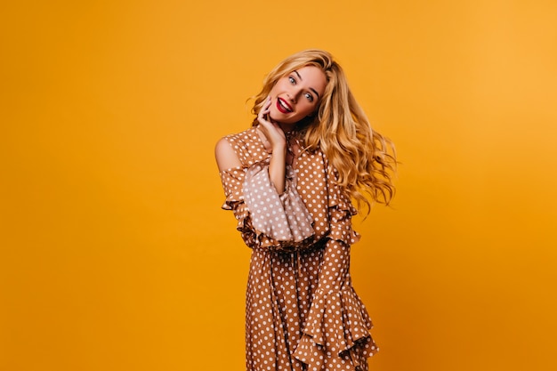 Jolie jeune femme s'amusant sur le mur jaune. Fille bouclée inspirée en robe rétro posant