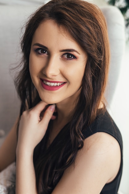 Jolie jeune femme s&#39;assoit souriant dans une chaise blanche douce