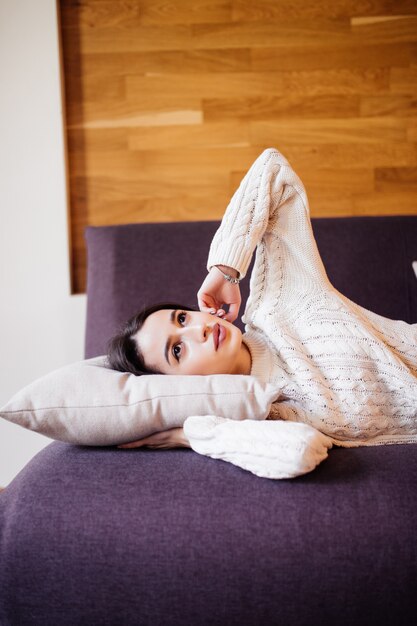 Jolie jeune femme s'est réveillée après une sieste quotidienne entre le travail à faire sur le canapé sombre dans un appartement à la mode